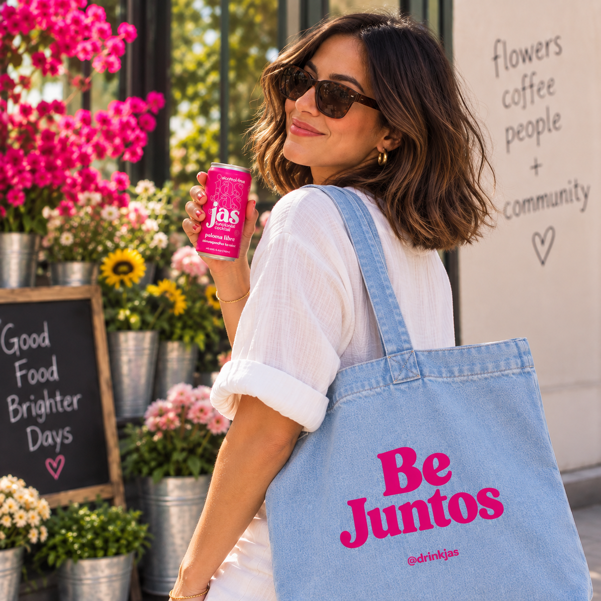 Woman carrying the Be Juntos denim tote on her shoulder outside a flower shop, holding a can of JAS Paloma Libre